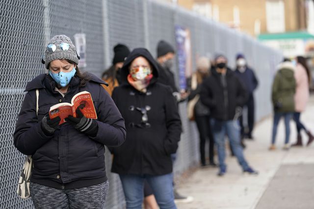 Ashley Gannon, left, reads a book as she and others wait in line outside a New York City Health + Hospitals COVID testing site in Brooklyn.